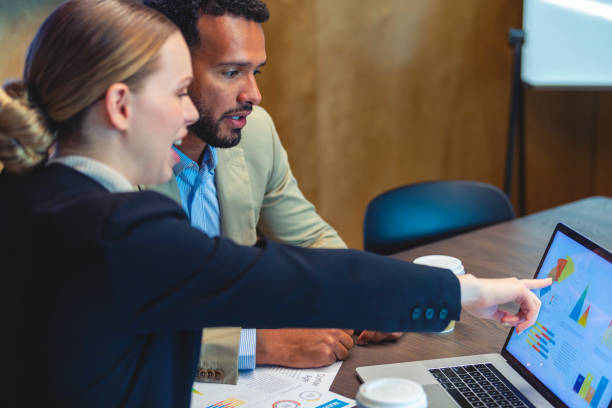Two colleagues in a meeting pointing at business charts on a laptop screen