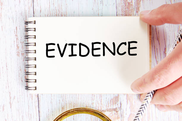 A hand writing the word EVIDENCE on a notepad next to a magnifying glass